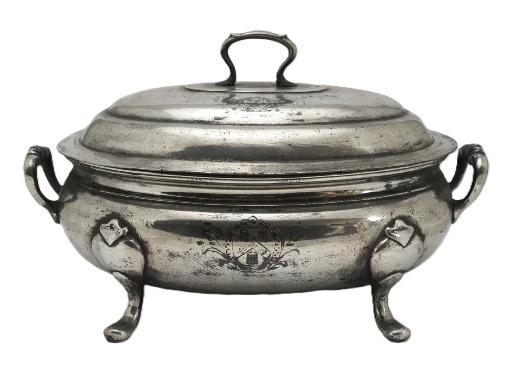 An antique Georgian pewter oval soup tureen featuring a domed lid with a loop handle, twin side handles, cabriole legs, and an engraved armorial crest.