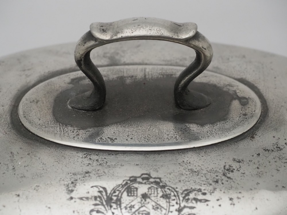 An antique Georgian pewter oval soup tureen featuring a domed lid with a loop handle, twin side handles, cabriole legs, and an engraved armorial crest. View VII