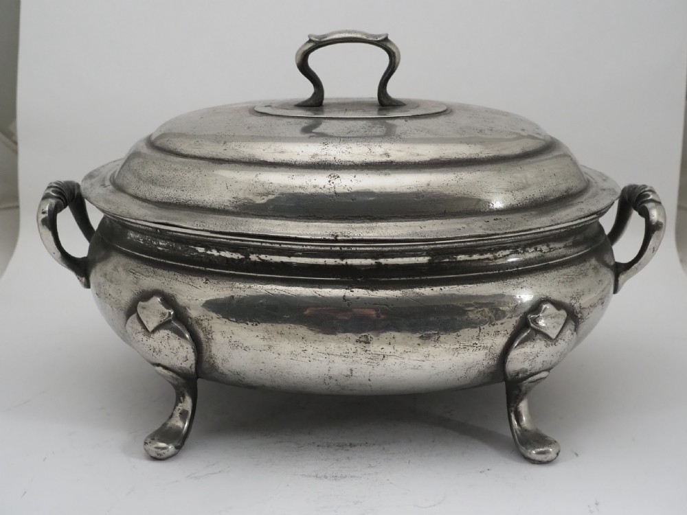 An antique Georgian pewter oval soup tureen featuring a domed lid with a loop handle, twin side handles, cabriole legs, and an engraved armorial crest. View X
