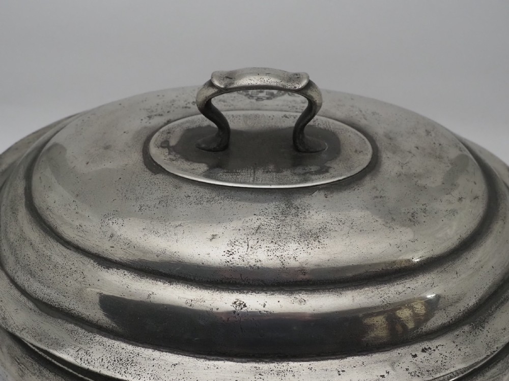 An antique Georgian pewter oval soup tureen featuring a domed lid with a loop handle, twin side handles, cabriole legs, and an engraved armorial crest. View XII