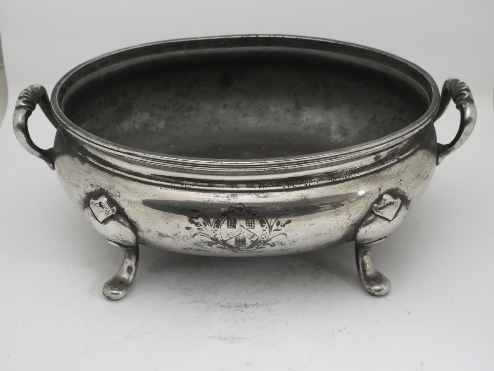 An antique Georgian pewter oval soup tureen featuring a domed lid with a loop handle, twin side handles, cabriole legs, and an engraved armorial crest. View XIII