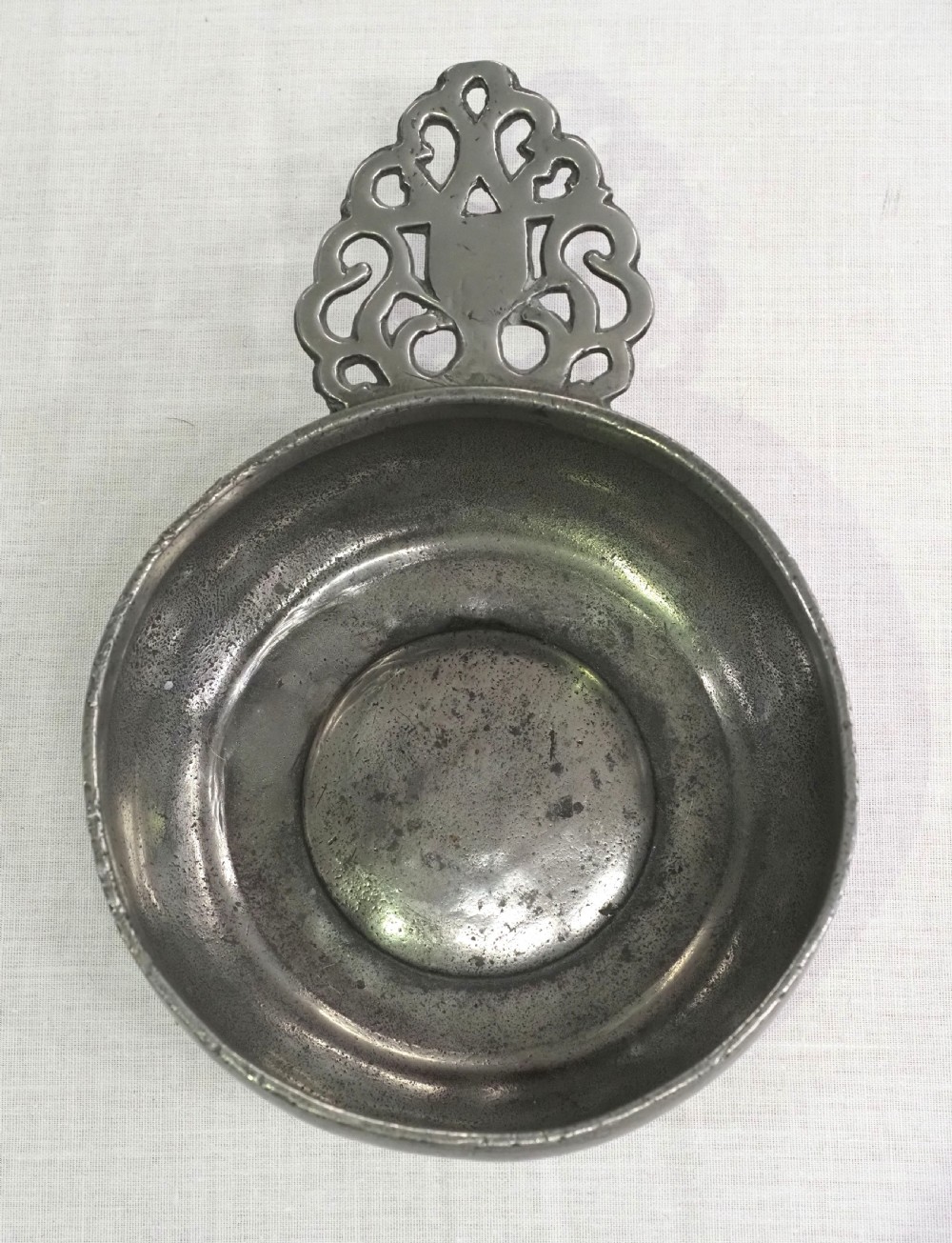 An antique silver-grey pewter porringer bowl featuring a single ornate pierced scrollwork ear handle. View II