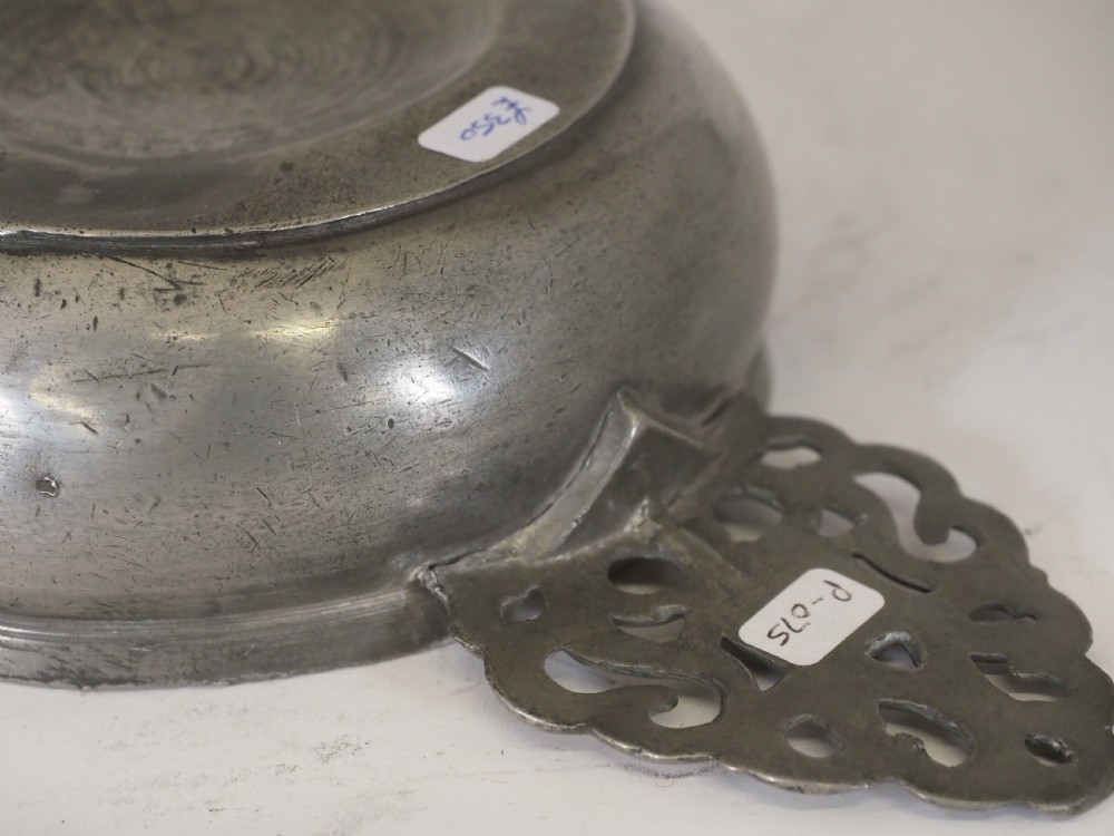 An antique silver-grey pewter porringer bowl featuring a single ornate pierced scrollwork ear handle. View V