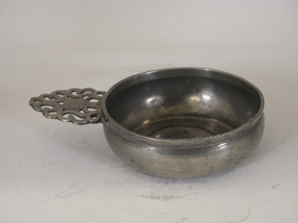An antique silver-grey pewter porringer bowl featuring a single ornate pierced scrollwork ear handle. View VII