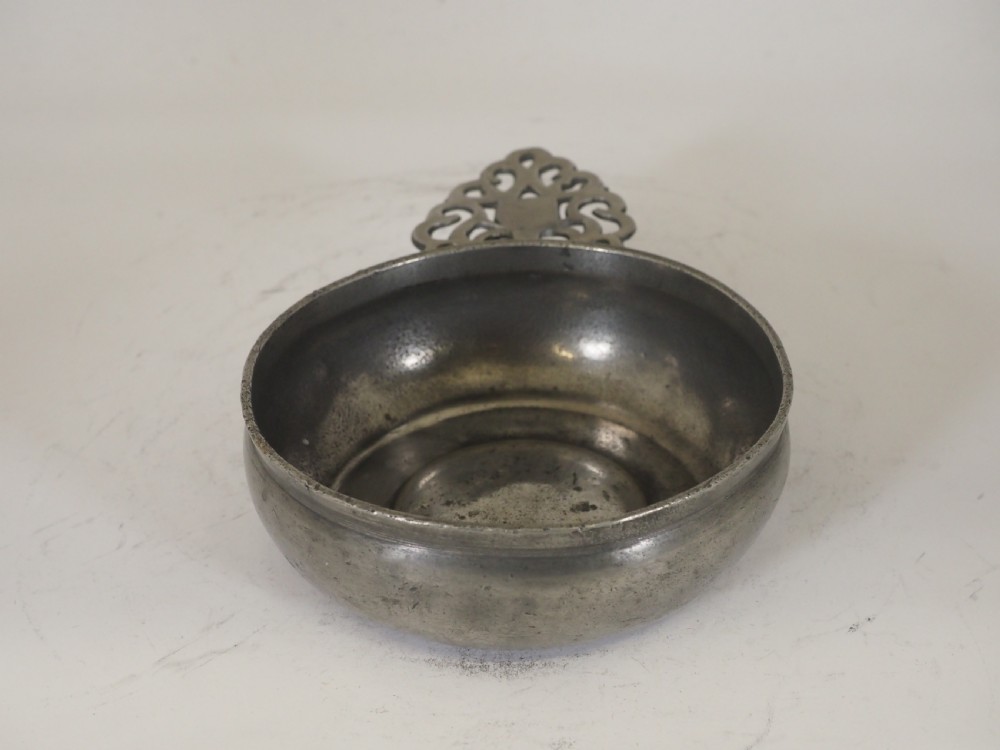 An antique silver-grey pewter porringer bowl featuring a single ornate pierced scrollwork ear handle. View VIII