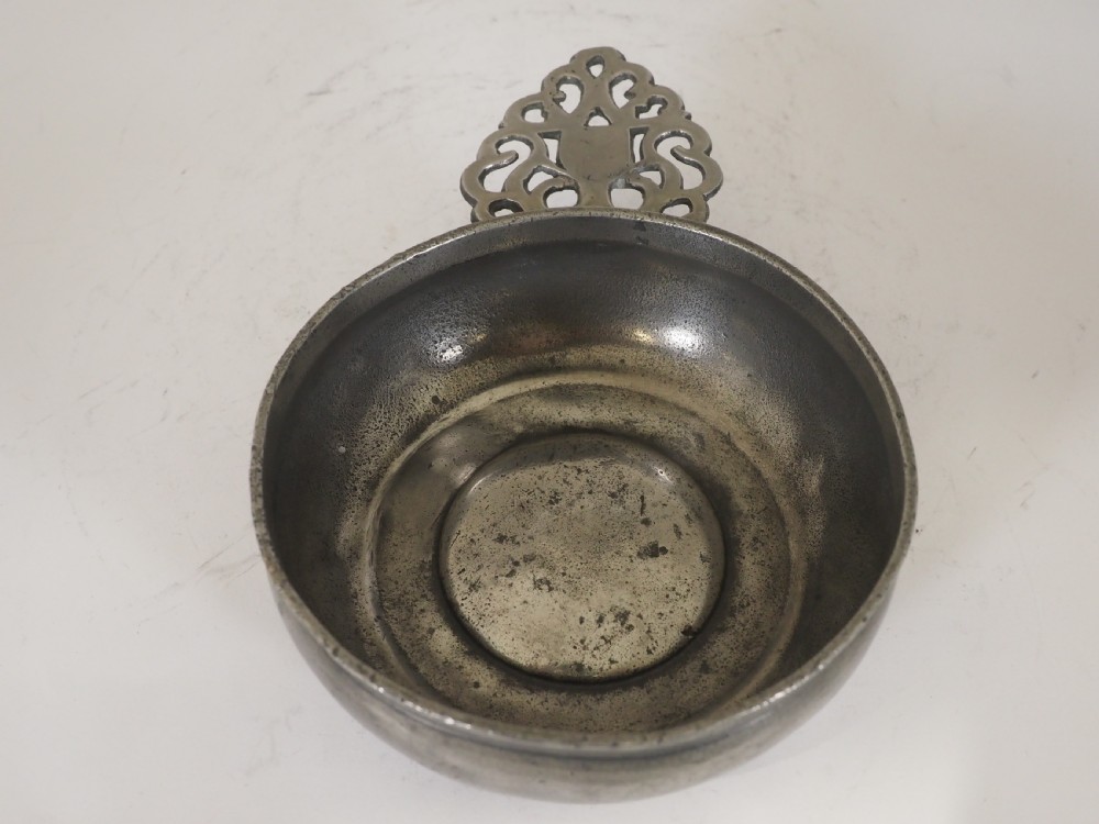 An antique silver-grey pewter porringer bowl featuring a single ornate pierced scrollwork ear handle. View X