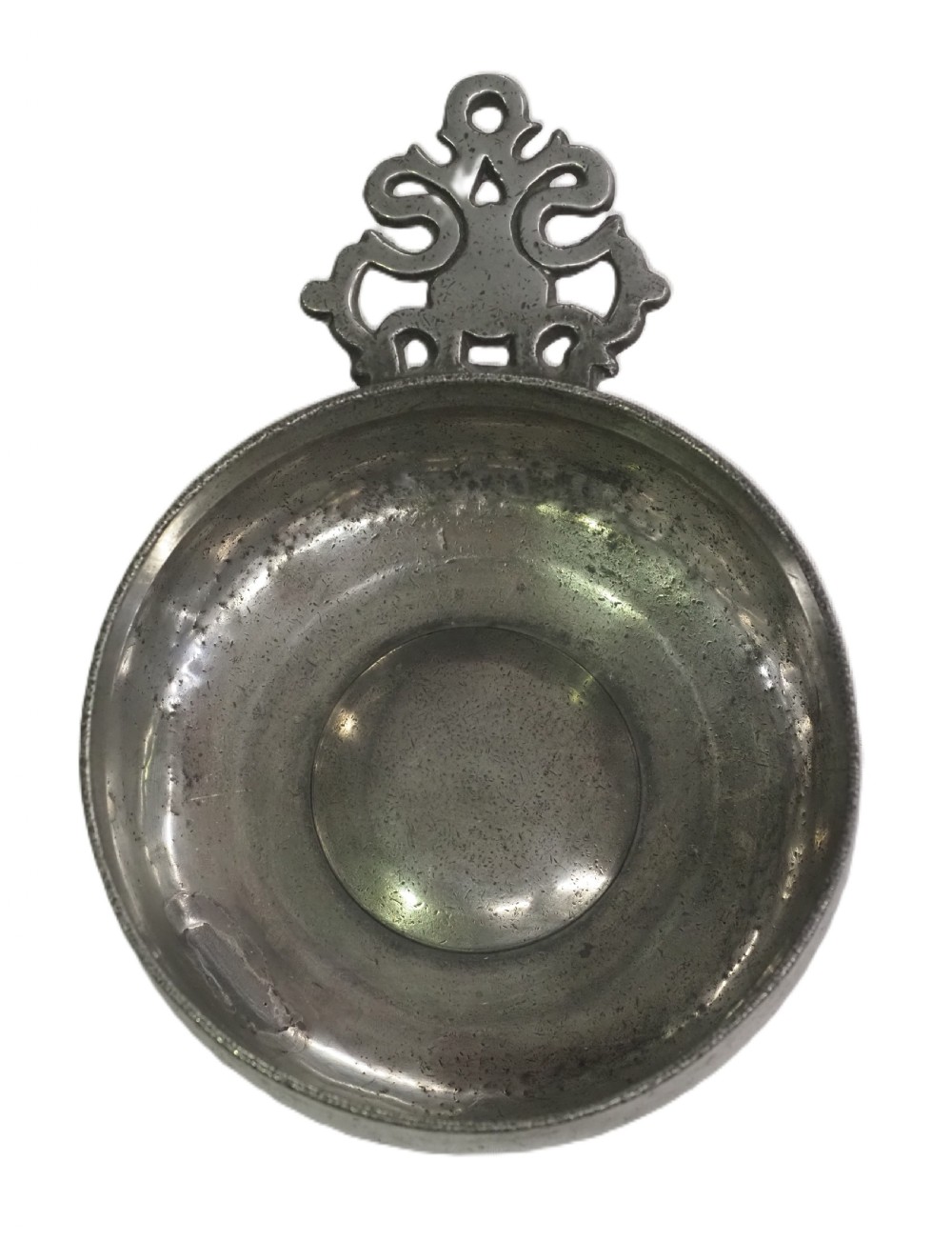 An antique circular pewter porringer bowl featuring a textured interior basin and a decorative pierced scrollwork handle.