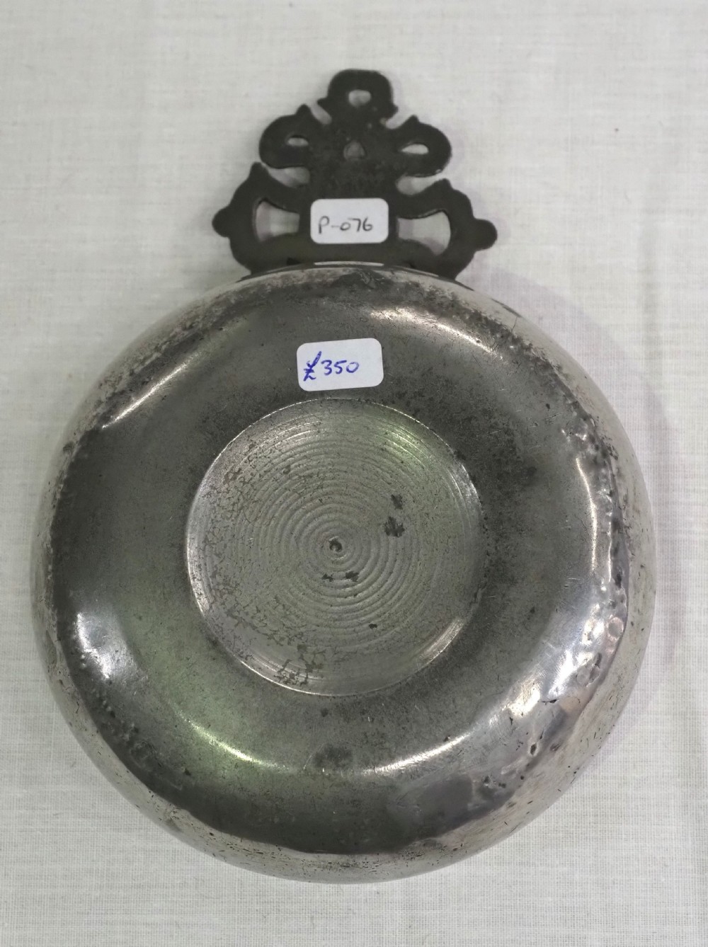 An antique circular pewter porringer bowl featuring a textured interior basin and a decorative pierced scrollwork handle. View III