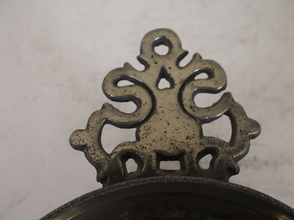 An antique circular pewter porringer bowl featuring a textured interior basin and a decorative pierced scrollwork handle. View VI