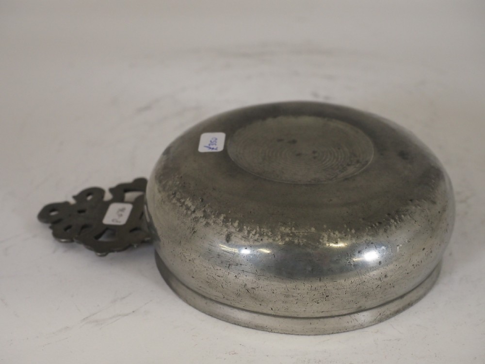 An antique circular pewter porringer bowl featuring a textured interior basin and a decorative pierced scrollwork handle. View IX