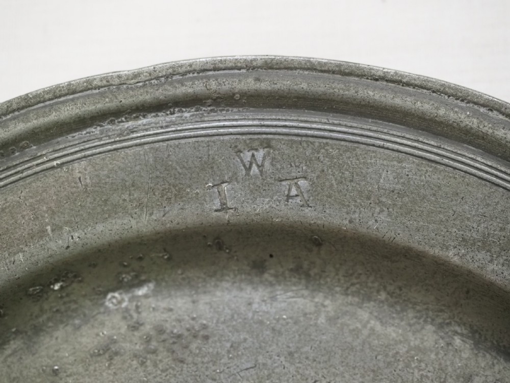 A circular 17th-century English pewter plate displaying a multiple reeded rim with stamped hallmarks near the top edge and initial stamps near the bottom. View III