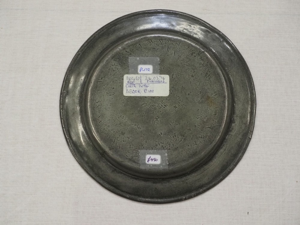 A circular 17th-century English pewter plate displaying a multiple reeded rim with stamped hallmarks near the top edge and initial stamps near the bottom. View IV