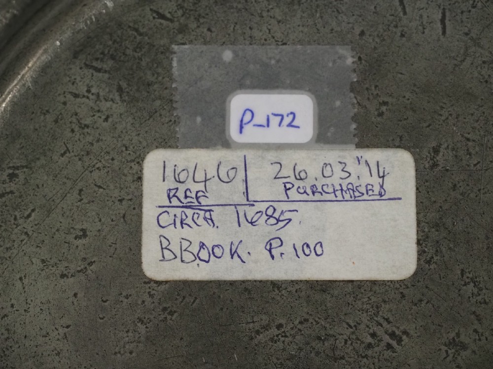 A circular 17th-century English pewter plate displaying a multiple reeded rim with stamped hallmarks near the top edge and initial stamps near the bottom. View VI