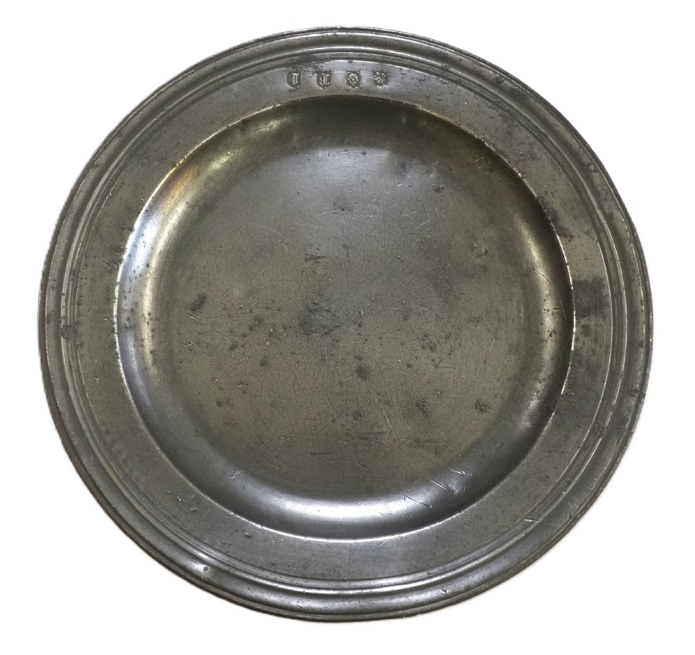 A circular antique pewter plate with a triple reeded rim and stamped touchmarks along the upper border.