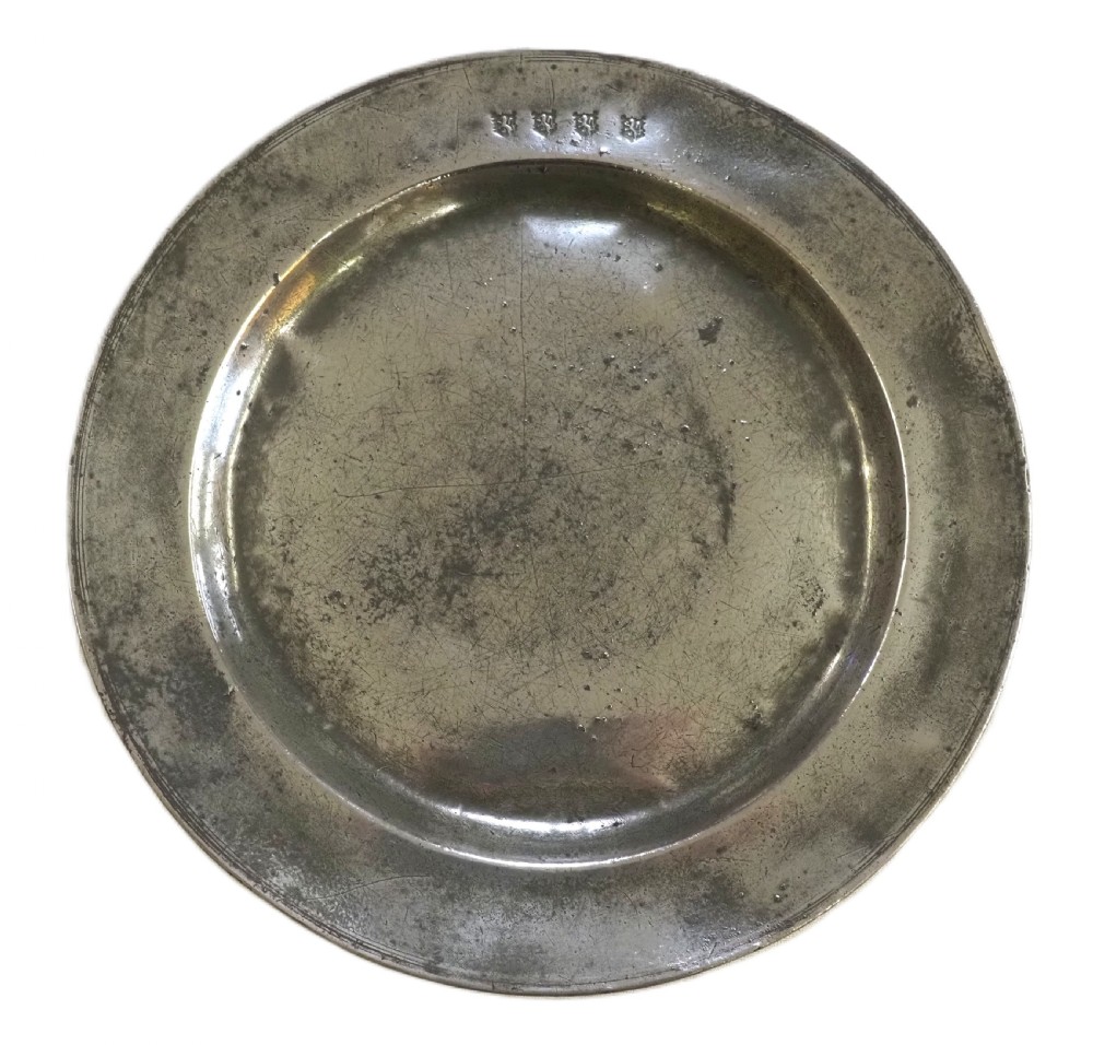 A circular 17th-century English pewter plate featuring an incised rim detail and stamped touchmarks along the upper border.