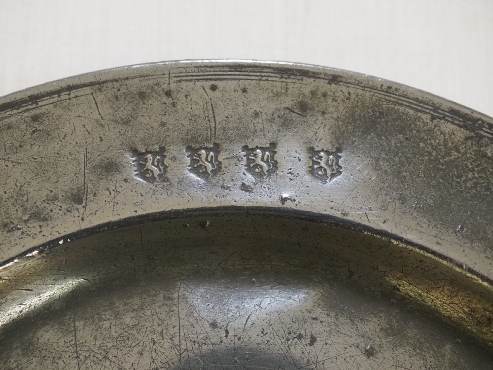 A circular 17th-century English pewter plate featuring an incised rim detail and stamped touchmarks along the upper border. View II