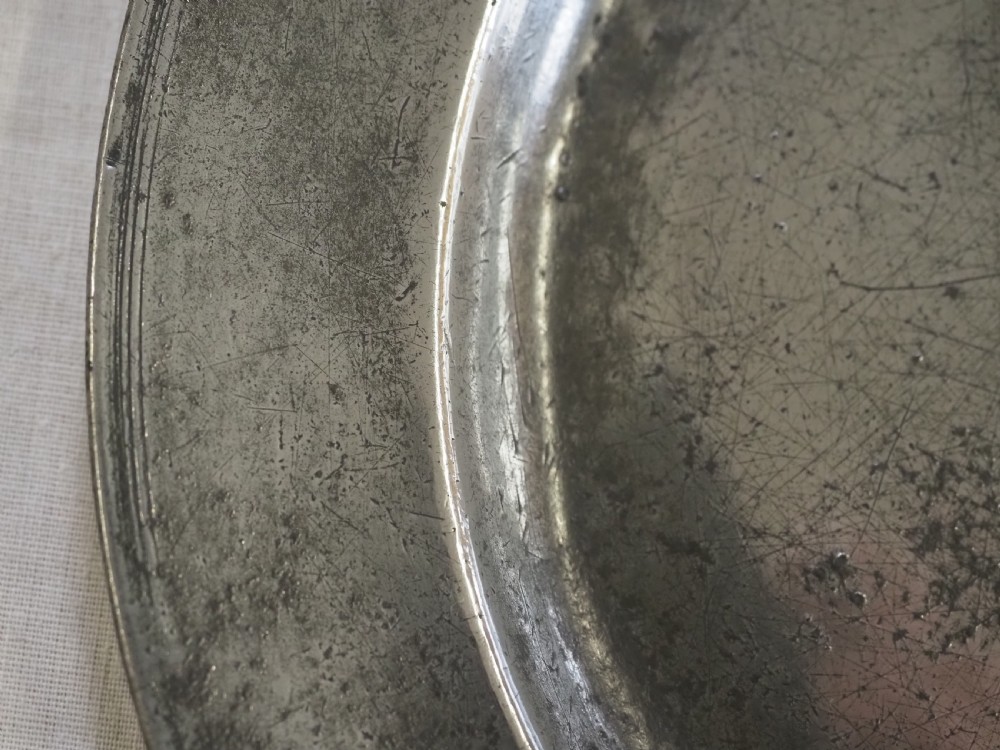 A circular 17th-century English pewter plate featuring an incised rim detail and stamped touchmarks along the upper border. View III