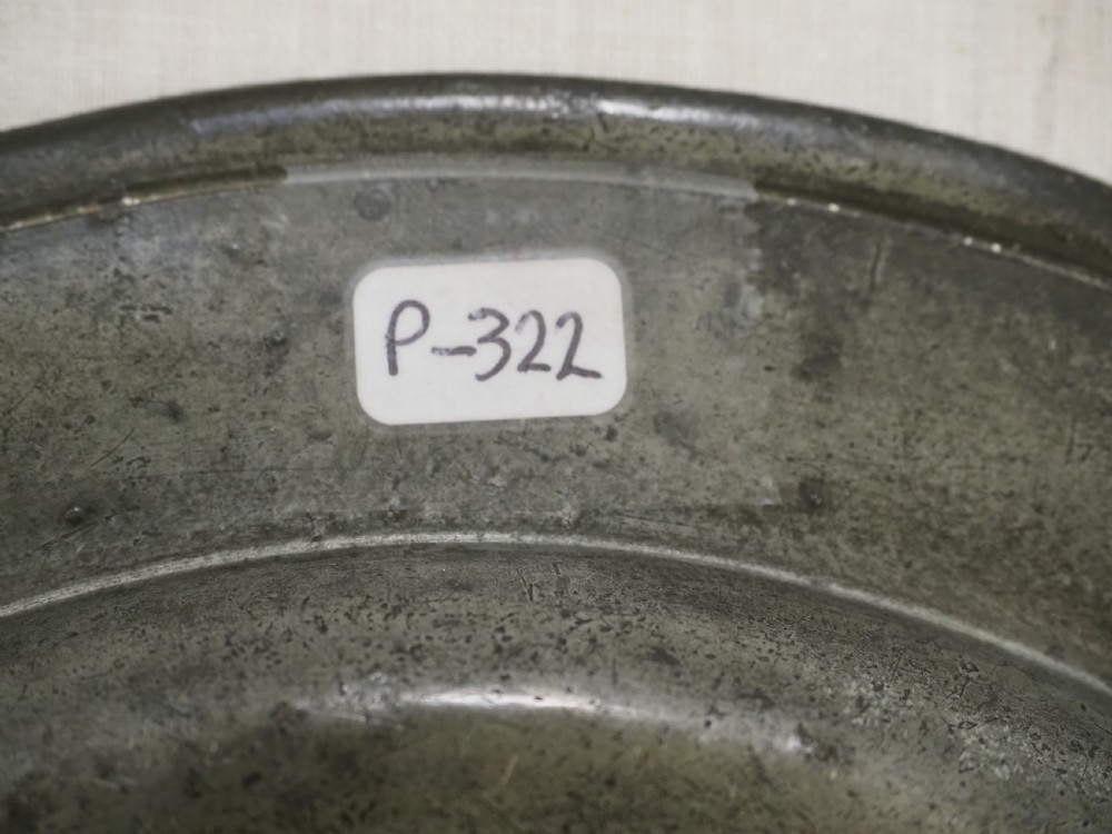 A circular 17th-century English pewter plate featuring an incised rim detail and stamped touchmarks along the upper border. View IV