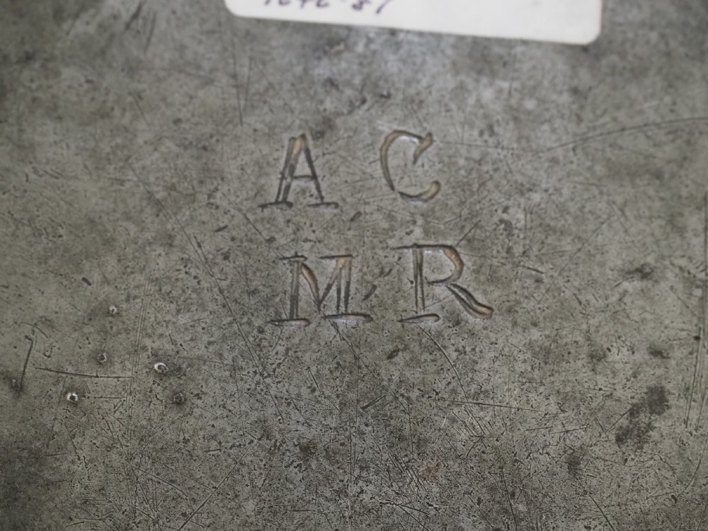 A circular 17th-century English pewter plate featuring an incised rim detail and stamped touchmarks along the upper border. View V
