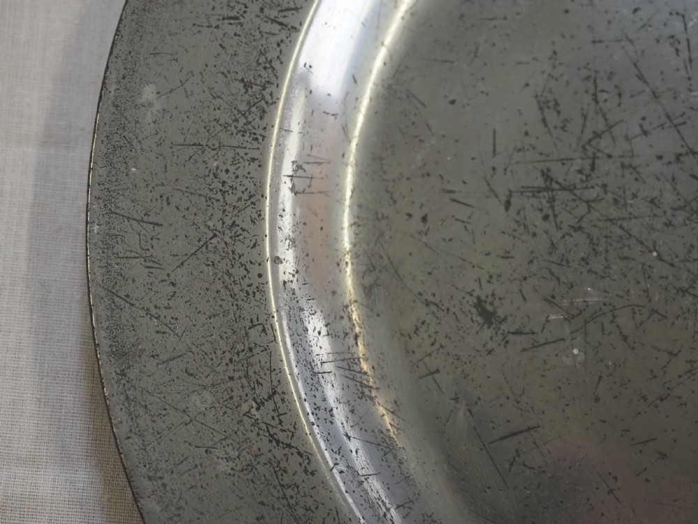 A circular 18th-century English pewter plate with a broad rim featuring a small stamped coat of arms at the top. View III