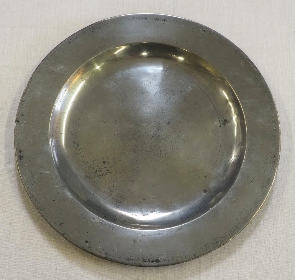 A circular antique pewter plate featuring a wide plain rim, a central shallow well, and subtle surface wear with a silver-grey patina.