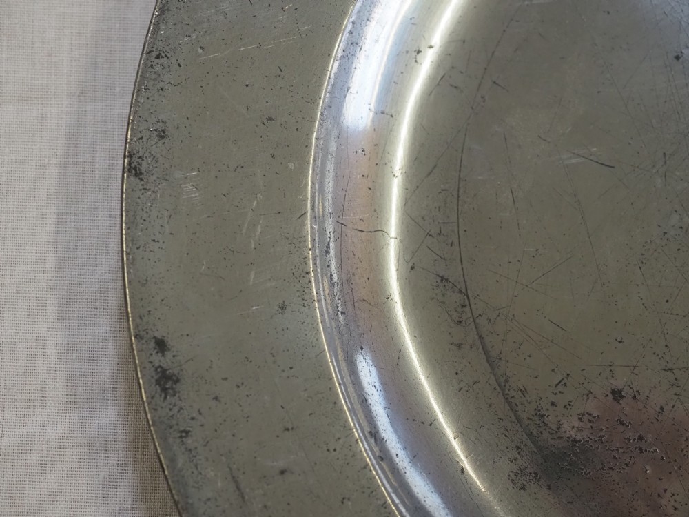 A circular antique pewter plate featuring a wide plain rim, a central shallow well, and subtle surface wear with a silver-grey patina. View II