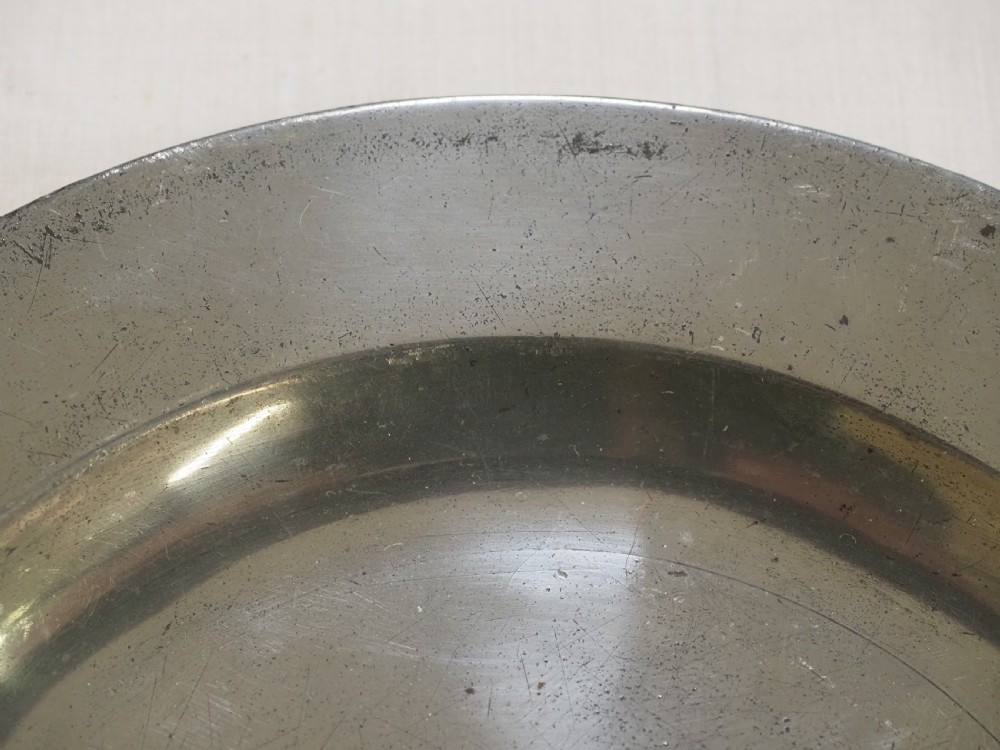 A circular antique pewter plate featuring a wide plain rim, a central shallow well, and subtle surface wear with a silver-grey patina. View III