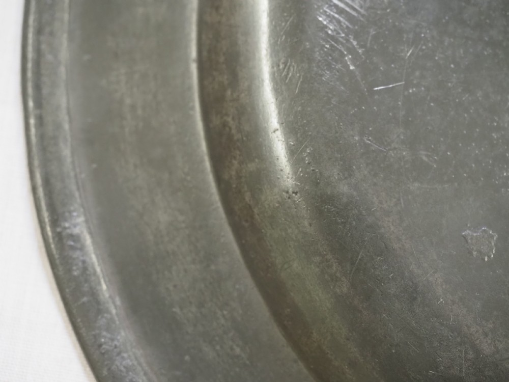 A circular antique pewter plate featuring a wide plain rim, a central shallow well, and subtle surface wear with a silver-grey patina. View IX