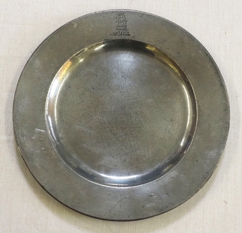 An 18th-century circular English pewter plate with a wide plain rim featuring an engraved lion crest at the top.