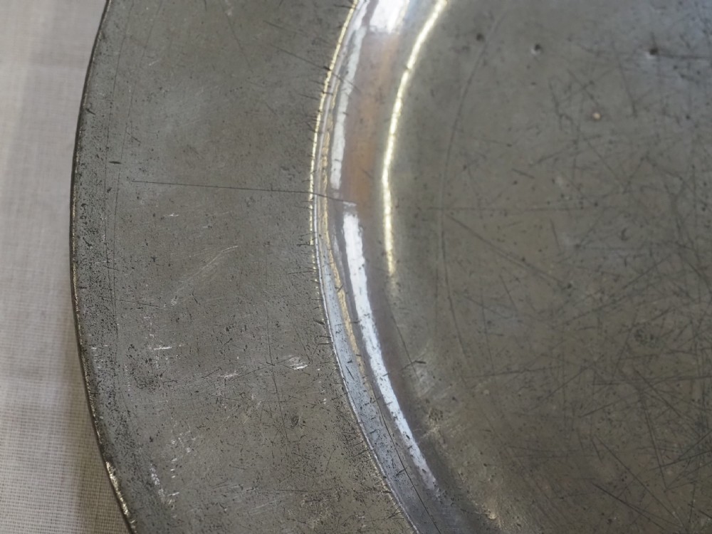 An 18th-century circular English pewter plate with a wide plain rim featuring an engraved lion crest at the top. View III