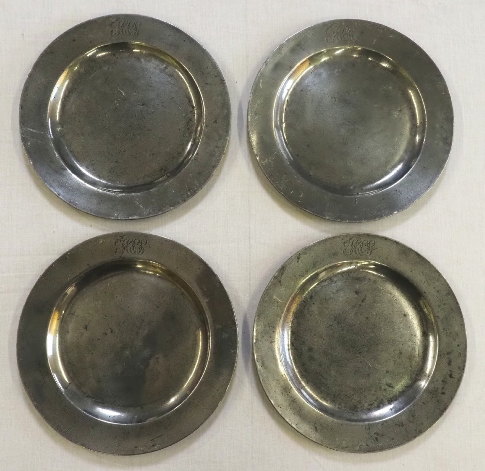 A set of four circular antique pewter plates featuring engraved monograms along the upper rims and a naturally aged grey surface.