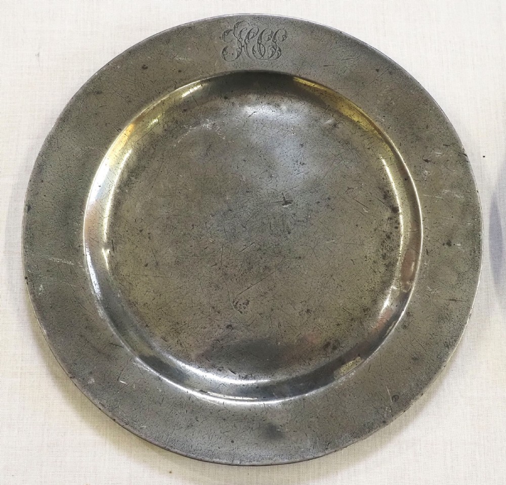 A set of four circular antique pewter plates featuring engraved monograms along the upper rims and a naturally aged grey surface. View II