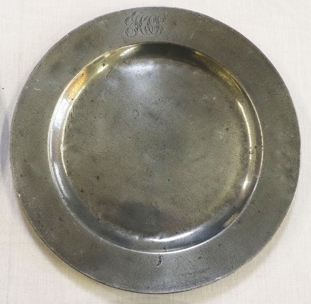 A set of four circular antique pewter plates featuring engraved monograms along the upper rims and a naturally aged grey surface. View III