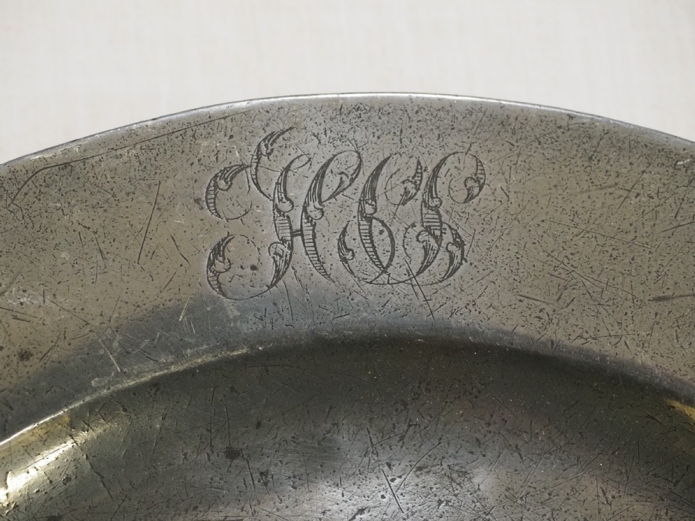 A set of four circular antique pewter plates featuring engraved monograms along the upper rims and a naturally aged grey surface. View V