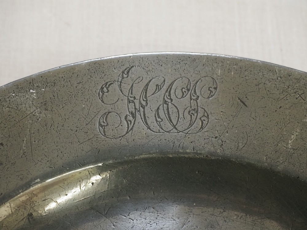 A set of four circular antique pewter plates featuring engraved monograms along the upper rims and a naturally aged grey surface. View VI
