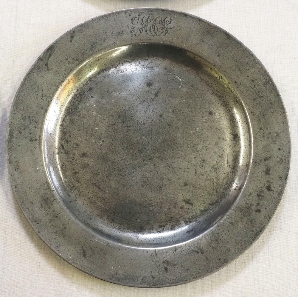 A set of four circular antique pewter plates featuring engraved monograms along the upper rims and a naturally aged grey surface. View VII