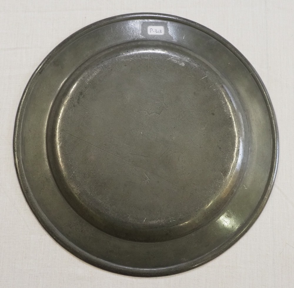 A set of four circular antique pewter plates featuring engraved monograms along the upper rims and a naturally aged grey surface. View IX