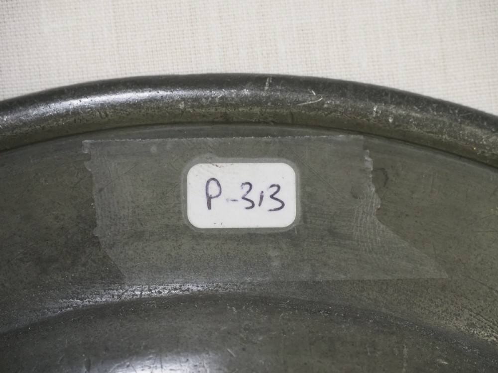 A set of four circular antique pewter plates featuring engraved monograms along the upper rims and a naturally aged grey surface. View XIII