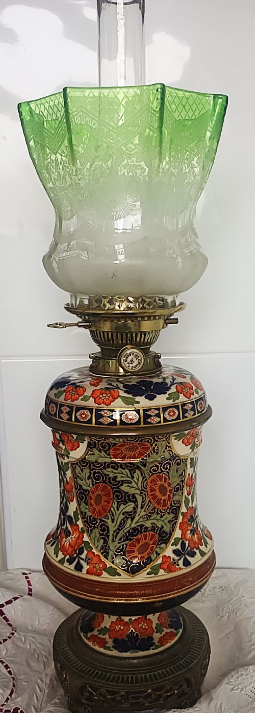 fig 1. A Victorian ceramic oil lamp featuring an etched pink glass shade, brass Duplex burner mechanism, and hand-painted floral ceramic body on a metal base.