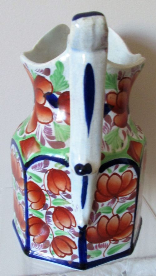 fig 1. An antique octagonal earthenware jug featuring hand-painted orange floral motifs, cobalt blue borders, green foliage, and a molded handle.
