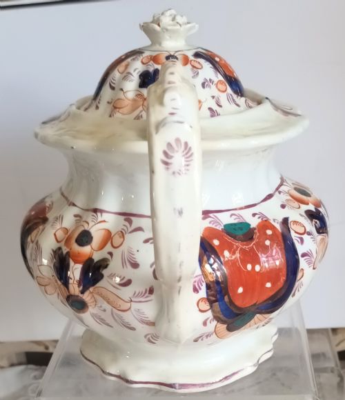 fig 1. An antique Georgian earthenware teapot featuring a hexagonal fluted shape, hand-painted rust red and cobalt blue motifs with lustre highlights, a curved spout, and a finial lid.