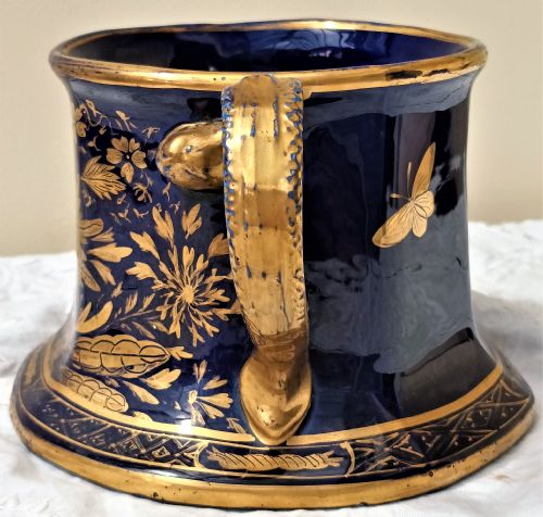 fig 1. An antique cobalt blue ironstone mug featuring flared sides, a gilded scroll handle, and intricate gold floral motifs with a geometric border.
