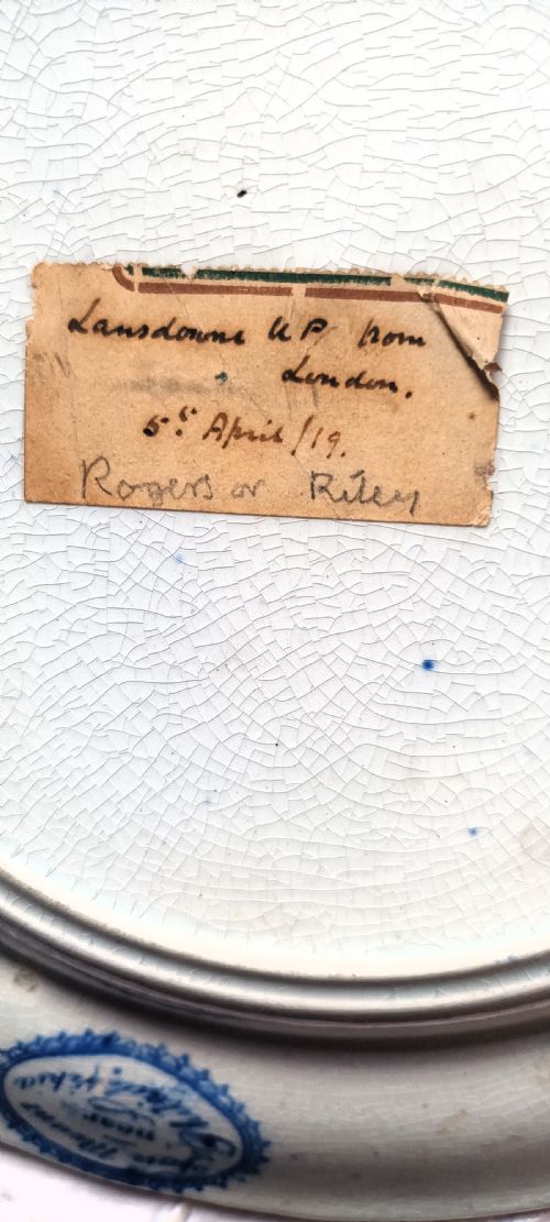 fig 2. An antique circular blue and white transfer-printed earthenware plate featuring a central landscape scene surrounded by a wide floral border.