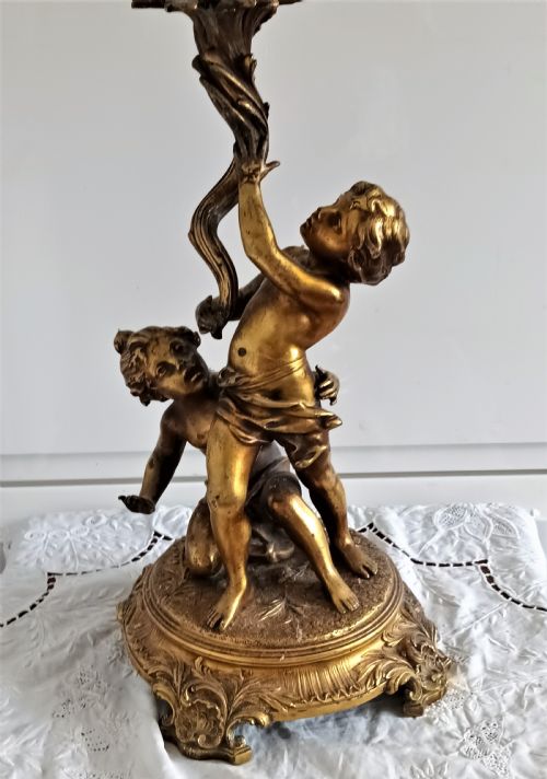 fig 2. An antique Victorian oil lamp featuring a gilded metal base with sculpted cherubs, a green glass reservoir, and a yellow ruffled glass shade with chimney.