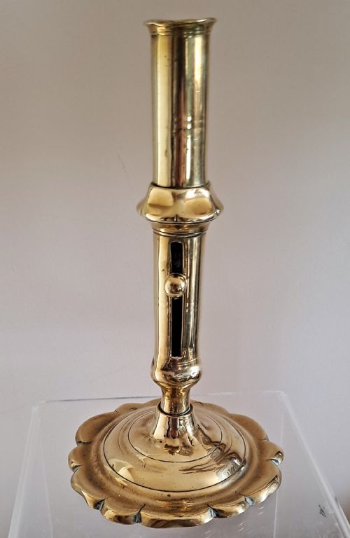 fig 1. A polished gold-toned brass candlestick featuring a scalloped petal base, knopped stem, and a side candle ejector mechanism.