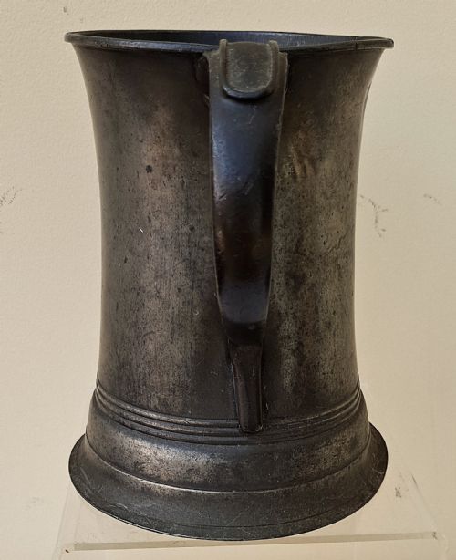 fig 1. An antique Victorian pewter quart mug featuring a concave body, a flared moulded base, and a dark curved handle.