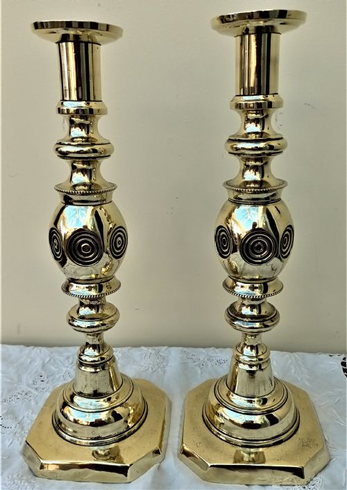 fig 1. A pair of polished Victorian brass candlesticks featuring turned stems with concentric circle motifs and octagonal bases stamped with good luck text.