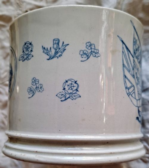 fig 1. A white ceramic mug decorated with blue transfer-printed portraits of King Edward VII and Queen Alexandra alongside heraldic emblems.