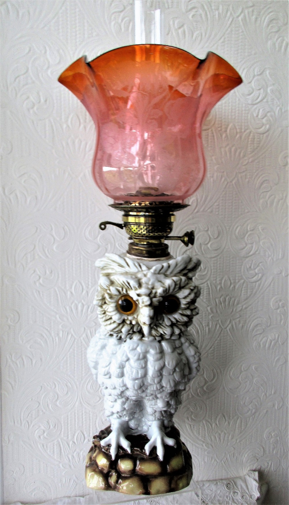 An antique Victorian Sitzendorf oil lamp featuring a sculpted white glazed porcelain owl base with glass eyes, brass burner, clear glass chimney, and a flared, etched pink glass shade.