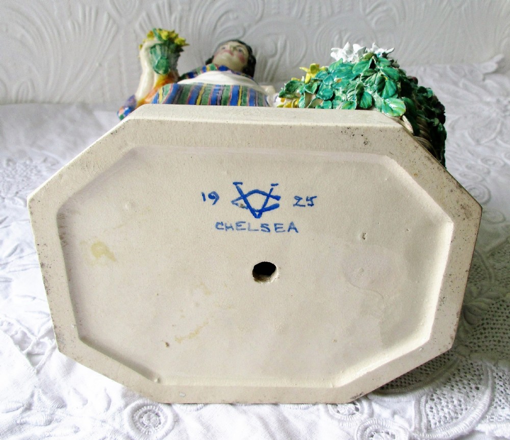 A glazed ceramic figurine depicting a female flower vendor holding a bunch of yellow daffodils next to a basket of flowers on an octagonal base. View V